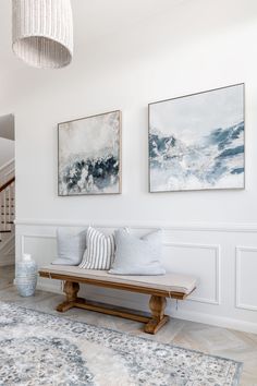 two paintings hang on the wall next to a bench in a room with white walls