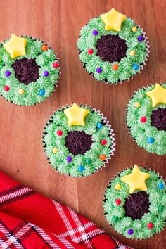 cupcakes decorated with green and purple frosting on a wooden table next to a plaid napkin