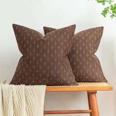 two brown pillows sitting on top of a wooden bench next to a plant and blanket