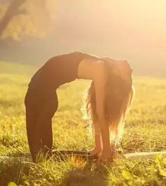 a woman bending over in the grass with her head down and hands behind her back