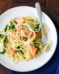 pasta with salmon and spinach on a white plate next to a silverware fork