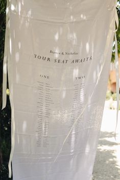 a white sheet hanging from the side of a tree in front of a sign that says your seat awaits one two