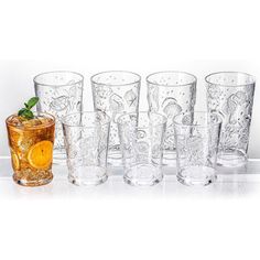 a set of six glasses with different designs on the glass and one filled with an orange slice