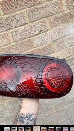 a person with tattoos holding up a red object in front of a brick wall that has pictures on it