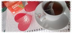 a cup of tea next to some heart shaped candies on a paper towel with a box of tesco's