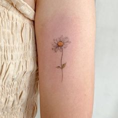 a woman's arm with a single daisy tattoo on it