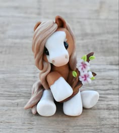 a small toy horse sitting on top of a wooden table with flowers in it's mouth