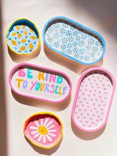 four small trays with painted designs on them and the words be kind to yourself