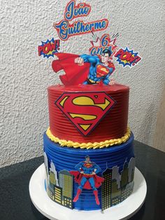 a superman birthday cake on a black table with white wall in the backround