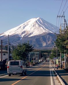 a car is driving down the street in front of a mountain with snow on it