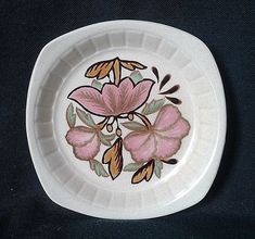 a white plate with pink flowers painted on the front and side, sitting on a black surface