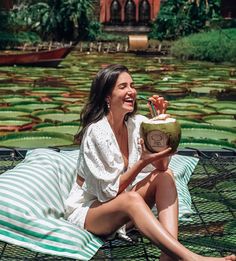 a woman sitting on the ground with a coconut drink in her hand and smiling at someone