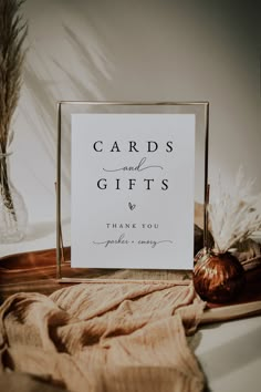 a card and gifts sign sitting on top of a table next to some dried plants