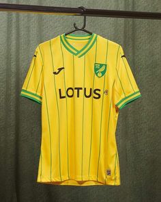 a yellow soccer jersey hanging on a clothes line in front of a green curtain with the word lotus printed on it