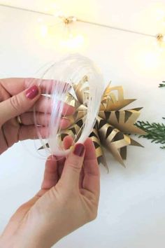 two hands are holding a wine glass with gold decorations on the wall behind it and christmas lights in the background