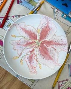 a white plate topped with a pink flower on top of a table next to markers and pencils