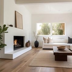 a living room with white furniture and a fire place in the fireplace, surrounded by wood flooring