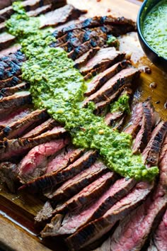 grilled steak with green sauce on wooden cutting board next to bowl of dipping sauce