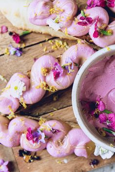 doughnuts with pink icing and flowers are on a wooden table next to bread