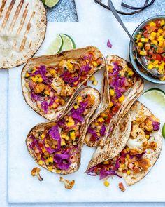 several tacos on a cutting board with limes and other food items around them