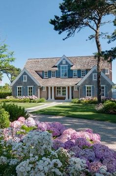 a house with blue shutters and white trim on the front, surrounded by flowers