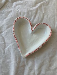 a white heart shaped dish with red writing on the bottom and inside, sitting on a bed sheet