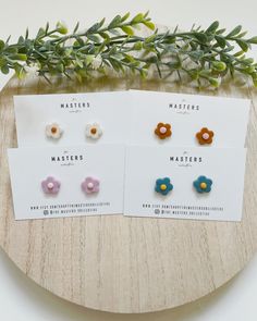 three different flower studs on top of a wooden table next to green leaves and flowers