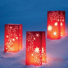 three red paper bags with white stars on them in the snow, one is lit up