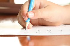 a child's hand is holding a pencil and writing on a piece of paper