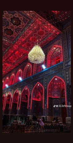 a chandelier hanging from the ceiling in a room with red lighting and intricate designs