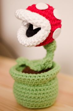 a crocheted red and white mushroom sitting on top of a green plant pot