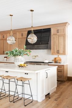 a kitchen island with four stools in front of it and two hanging lights above the island