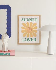 a white dresser topped with a lamp next to a painting and a framed sunflower