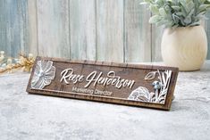 a wooden sign sitting on top of a table next to a vase filled with flowers