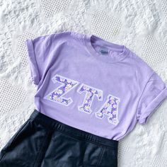 These classic and vintage-style letters are perfect for new and seasoned sorority women alike! Features double-stitched cottage-style purple daisy letters on a stark white background attached to a comfortable unisex lavender tee. This seller is licensed with Affinity Licensing to ensure a verified, quality product. Care Instructions: Machine wash cold, inside out; Tumble dry low; Low iron as needed Sorority Block Letters Shirts, Sorority Letters Shirt, Sorority Letter Shirt, Spring Lavender Letter Print Top, Spring Sorority Cotton T-shirt, Sorority Cotton T-shirt For Spring, Sorority Style Cotton T-shirt For Spring, Purple Pre-shrunk T-shirt For Spring, Cute Sorority Shirts