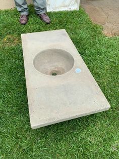 a man standing next to a concrete sink in the grass with his feet on the ground