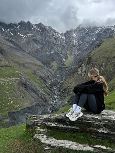 a woman sitting on top of a wooden bench in the mountains with snow covered mountains behind her