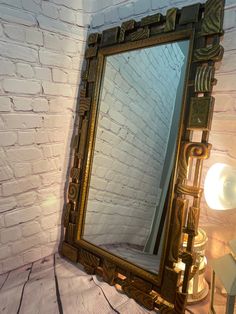 a mirror sitting on top of a wooden table next to a white brick wall and lamp