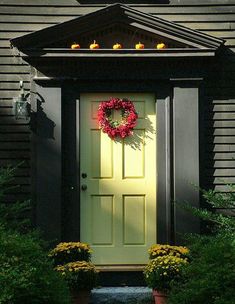 a green door with a wreath on it and some flowers in front of the door