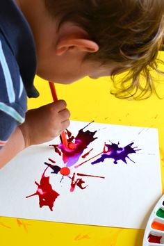 a young boy is painting with watercolors on paper and has his hands in the paint