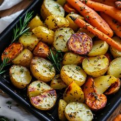 roasted potatoes and carrots with rosemary sprigs in a black tray on a table