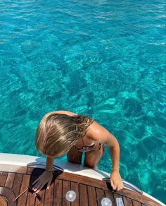 a woman standing on the back of a boat looking out at clear blue ocean water