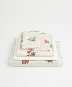 four pieces of white linen with red flowers and green scalloped edges, on top of each other