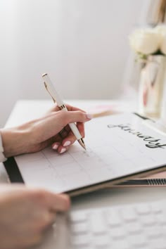 a person writing on a notepad with a pen in their hand and a flower vase behind them