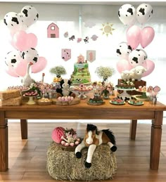 a table topped with lots of balloons and farm animals on top of hay bales