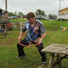 a man is playing with a hula hoop in the grass near a picnic table