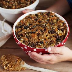 two hands holding a red and white bowl filled with granola