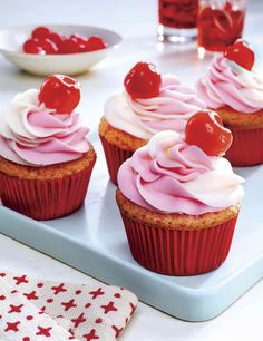 cupcakes with cherries and whipped cream are on a tray next to a bowl of cherries