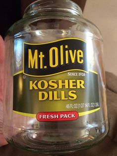 a person holding up a jar of kosher dills in their left hand, with the label on it