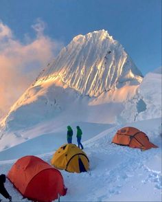 three tents pitched up in the snow with mountains in the back ground and people standing on top of them